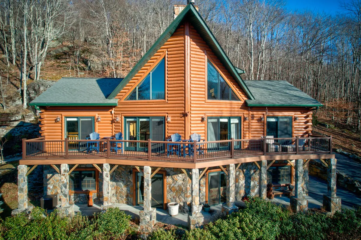 This image shows the log cabin's impressive exterior, featuring a spacious deck with stone pillars and surrounded by lush mountain nature. The view emphasizes the lodge’s mountain setting and the serene environment that greets guests upon arrival.