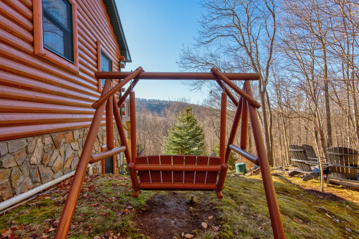 A peaceful outdoor scene featuring a wooden swing, Adirondack chairs, a stone wall, and panoramic mountain views. The inviting setting encourages relaxation, storytelling, and communal gatherings with friends after a day of exploring.