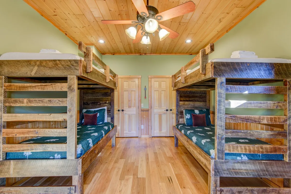 A welcoming bunk room with rustic wooden ceilings, sturdy wooden bunk beds, and green walls, offering a playful yet comfortable environment. The spaciousness and communal feel make it ideal for kids or teens to gather and create memories.