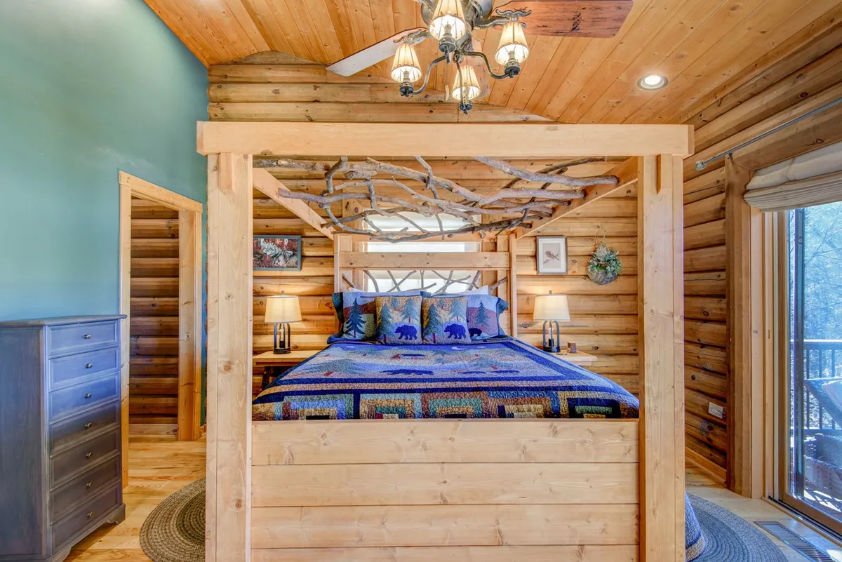 A serene bedroom featuring a canopy bed adorned with a colorful quilt, a wooden dresser, and large windows that allow natural light to fill the space. The atmosphere is inviting and tranquil, perfect for unwinding after a busy day.