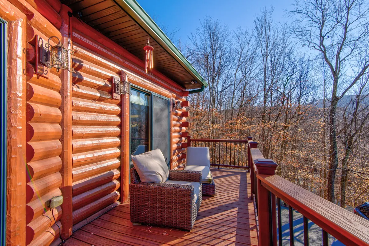 A cozy log cabin exterior with a welcoming outdoor seating area, surrounded by towering trees and gentle lantern lighting. The deck invites guests to enjoy sunrise coffee, evening conversations, and peaceful moments immersed in nature.
