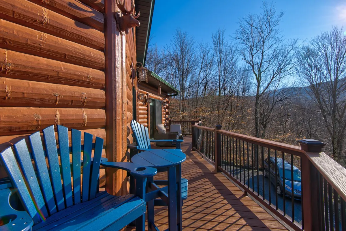The log cabin exterior framed by blue Adirondack chairs offers panoramic mountain views, inviting guests to relax and take in sunsets or plan their next day's adventure. The scene suggests both communal and tranquil moments in nature.