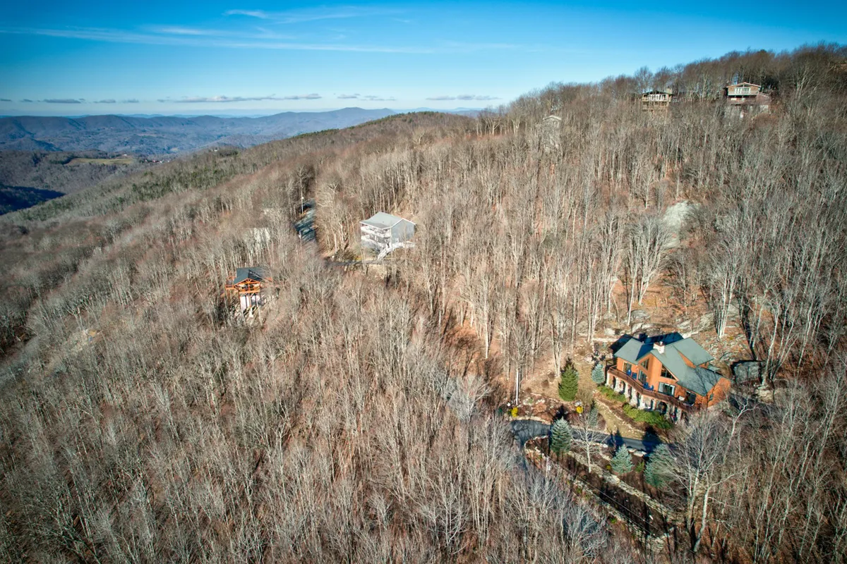 This tranquil view captures the main Carolina Elk Lodge house nestled among lush trees, with rolling distant mountains framing the background. The expansive outdoor setting suggests ample opportunities for stargazing, morning coffee, or enjoying the crisp mountain air.